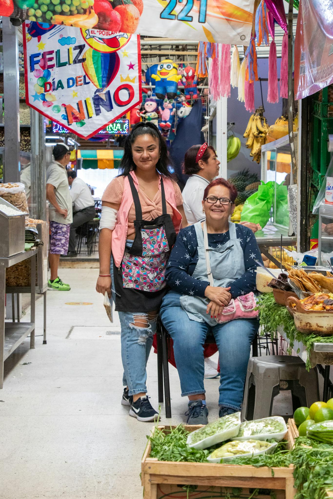 Two women selling fresh produce in a vibrant indoor market setting.
